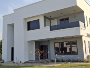 Modern two-story residential building with white exterior, grey accents, glass balcony railings, and manicured landscaping.