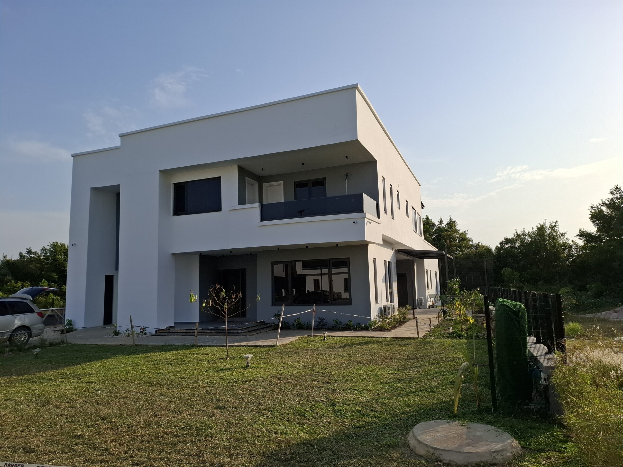 Modern two-story residential building with white exterior, grey accents, glass balcony railings, and manicured landscaping.