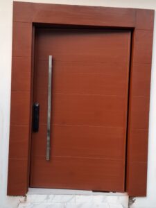 Modern solid wood front entrance door with a warm reddish stain, featuring horizontal grain panels, a long vertical stainless steel pull handle, and a black smart electronic lock.