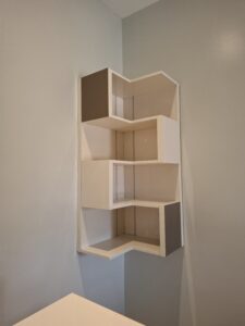 A 5-tier white zigzag floating corner shelf mounted on a light gray wall, ideal for minimalist home decor and small space storage.