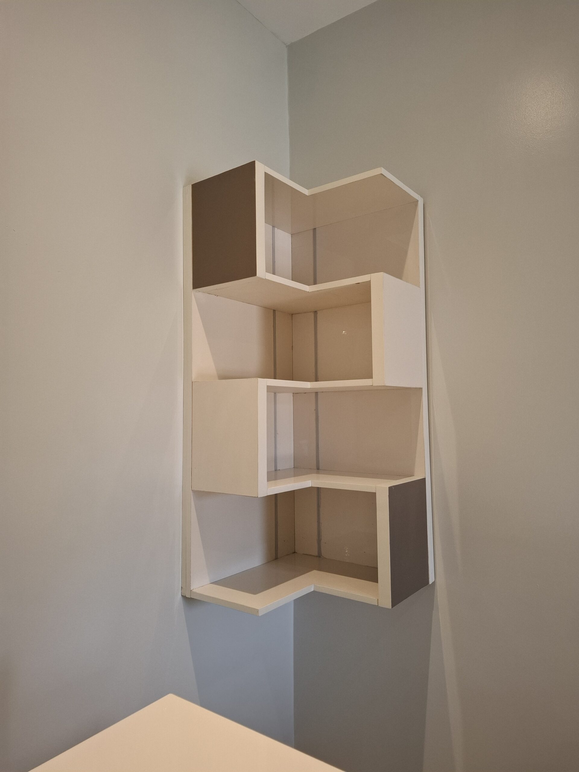 A 5-tier white zigzag floating corner shelf mounted on a light gray wall, ideal for minimalist home decor and small space storage.