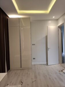 This is a modern, freestanding, two-door wardrobe in a glossy beige or off-white finish. 